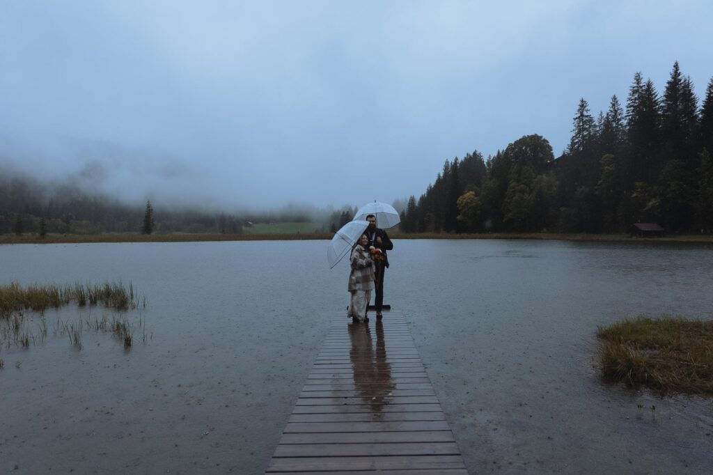 Couple with umbrellas standing on the dock at Lauenensee near Gstaad, Switzerland.