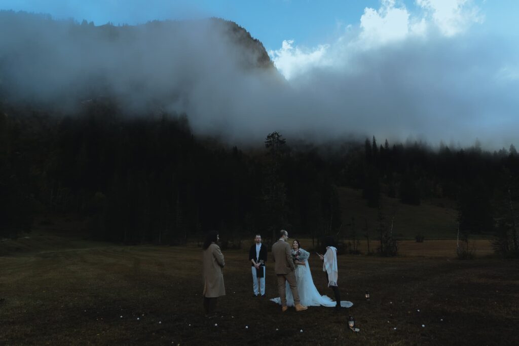 Elopement ceremony in a field at blue hour, in front of a small mountain surrounded by fog.