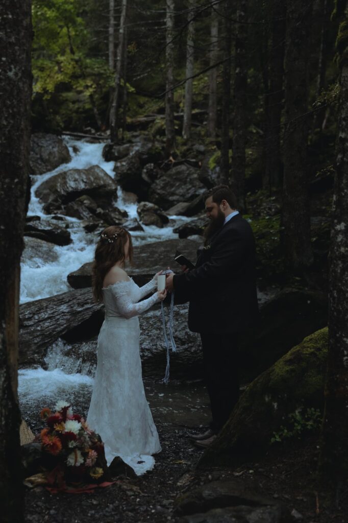 Couple doing a handfasting during their elopement ceremony, in front of a waterfall.