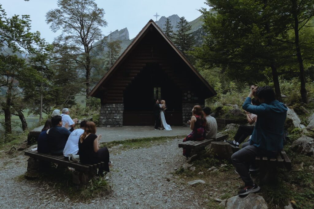 Guests sat in front of a chapel with mountains in the background, witnessing an elopement.