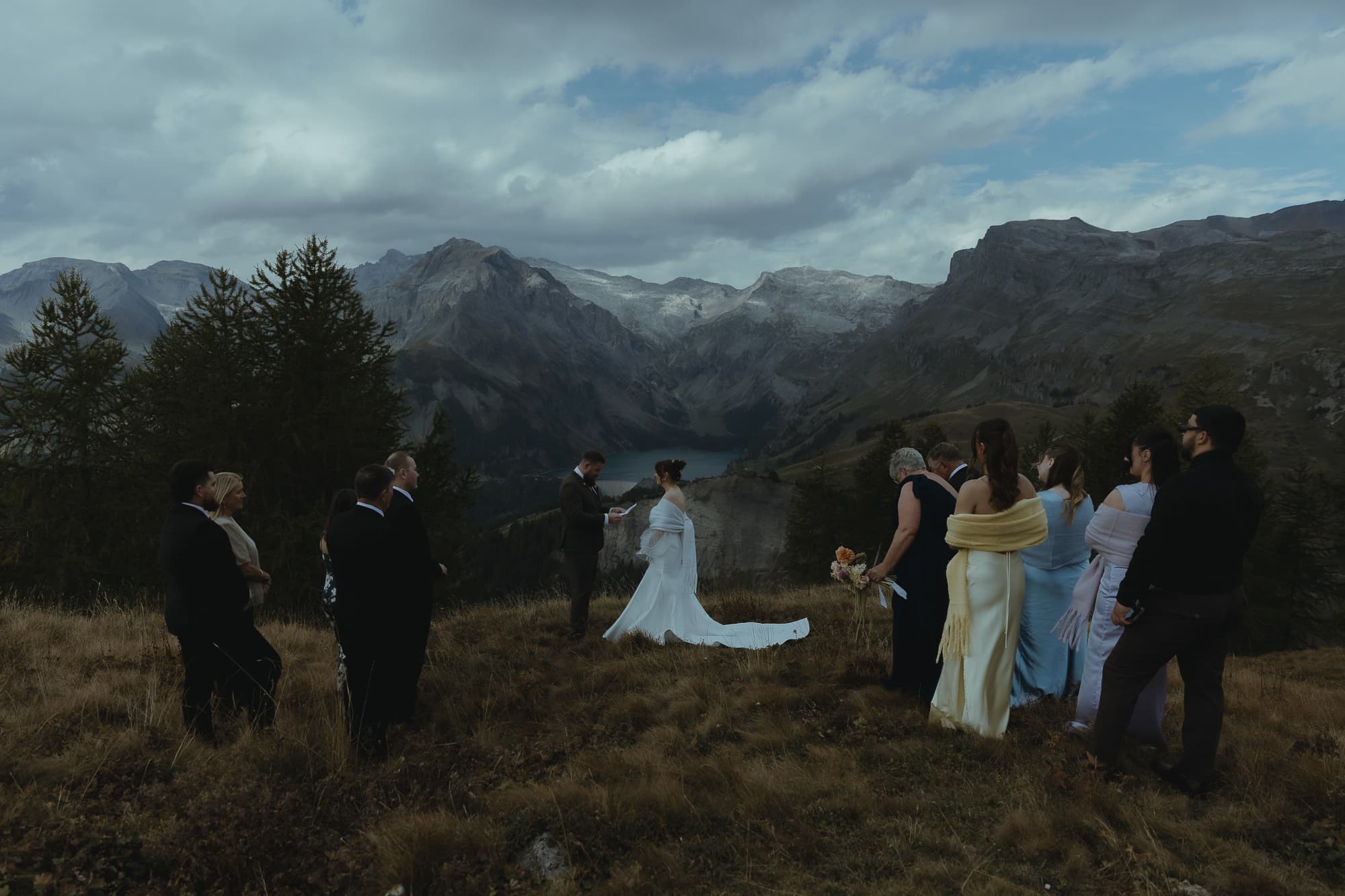 Guests standing on both sides of a couple, while they exchange elopement vows in front of an alpine scenery.