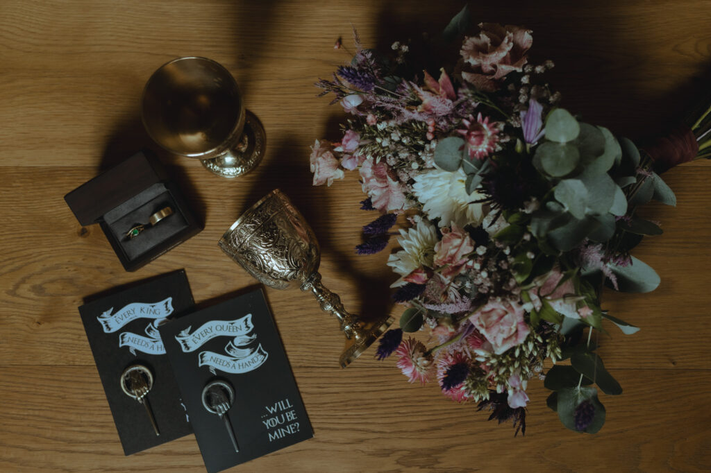 Fantasy inspired elopement details showing a bouquet, Game of Thrones pins, and rings.
