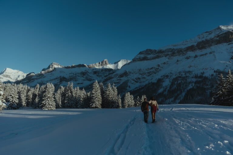 couple walking in a snowy landscape, in front of an impressive mountain range.