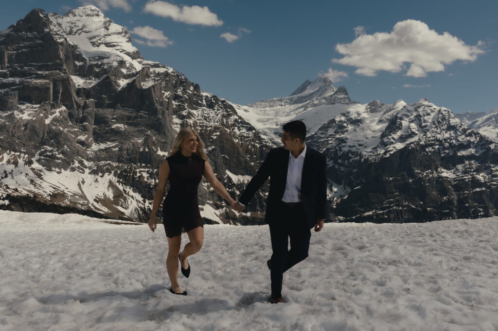 A couple walking in the snow and smiling at each other after their winter proposal near Grindelwald.